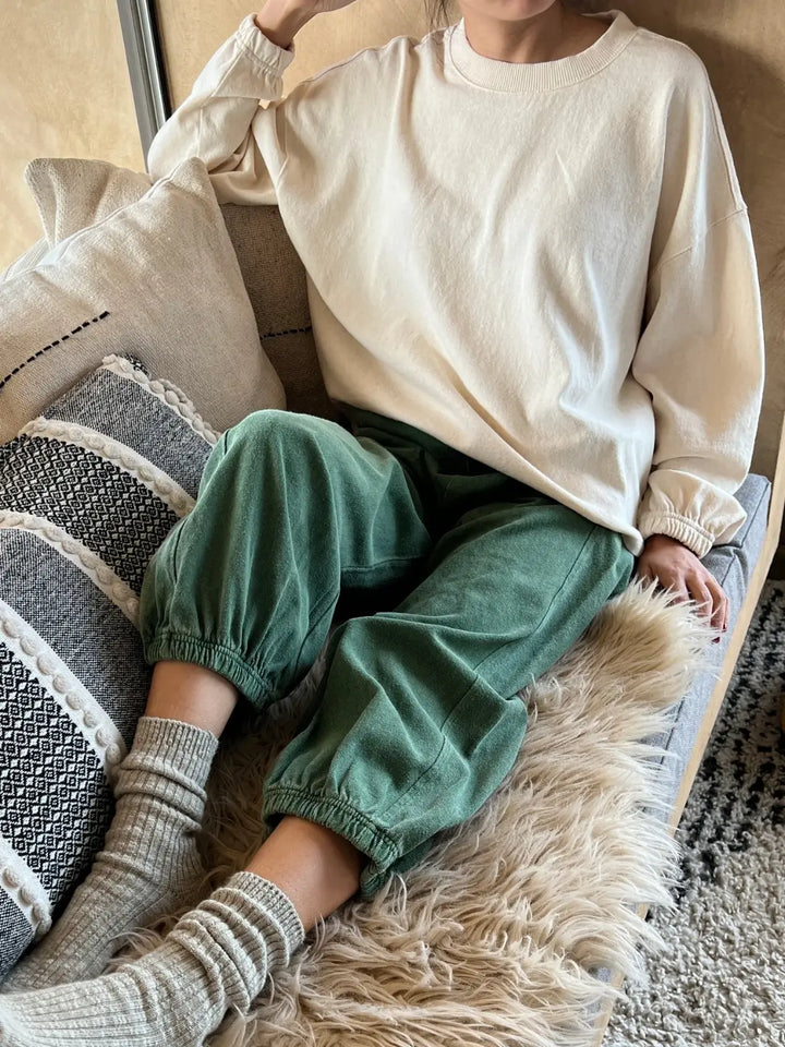 Person wearing a cream 'Naturelle Tee' sweater in 'Naturel' and green 'Balloon Pants' from Le Bon Shoppe sitting on a textured couch | Twentyseven Toronto