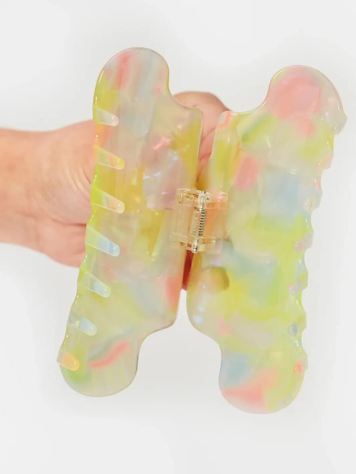 A hand holds open the translucent CHUNKS Nimbus Claw Clip in Sherbet Jelly, revealing its internal metal spring mechanism and colourful pastel patterns | Twentyseven Toronto