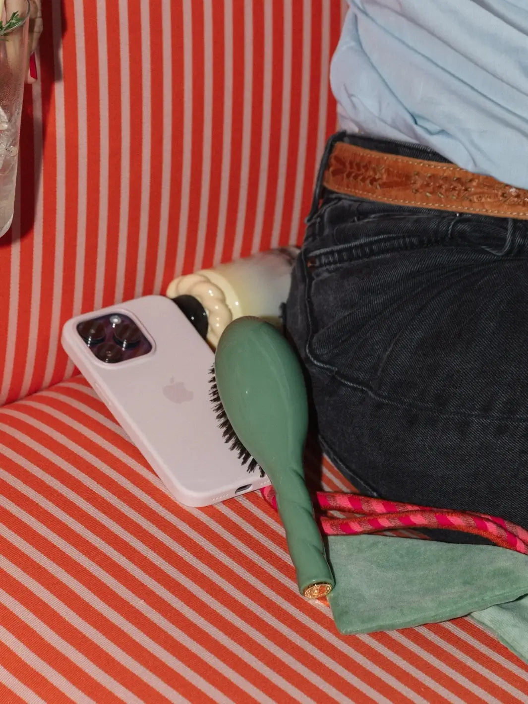 A lifestyle shot shows the La Bonne Brosse N.01 The Shine & Care Hairbrush The Universal Brush in Almond Green resting on a red and white striped surface next to a smartphone and a person in denim | Twentyseven Toronto