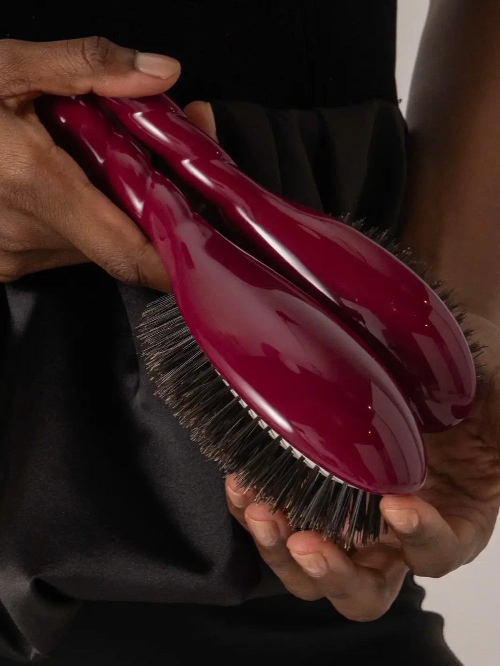 A person holds two La Bonne Brosse N.01 The Shine & Care Hairbrush The Universal Brush in Cherry Red models, showcasing the glossy finish and dense bristle structure | Twentyseven Toronto