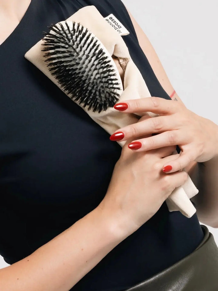 A person in a black top holds the La Bonne Brosse N.01 The Shine & Care Hairbrush The Universal Brush in Creamy White tucked inside its matching cream-colored protective pouch | Twentyseven Toronto