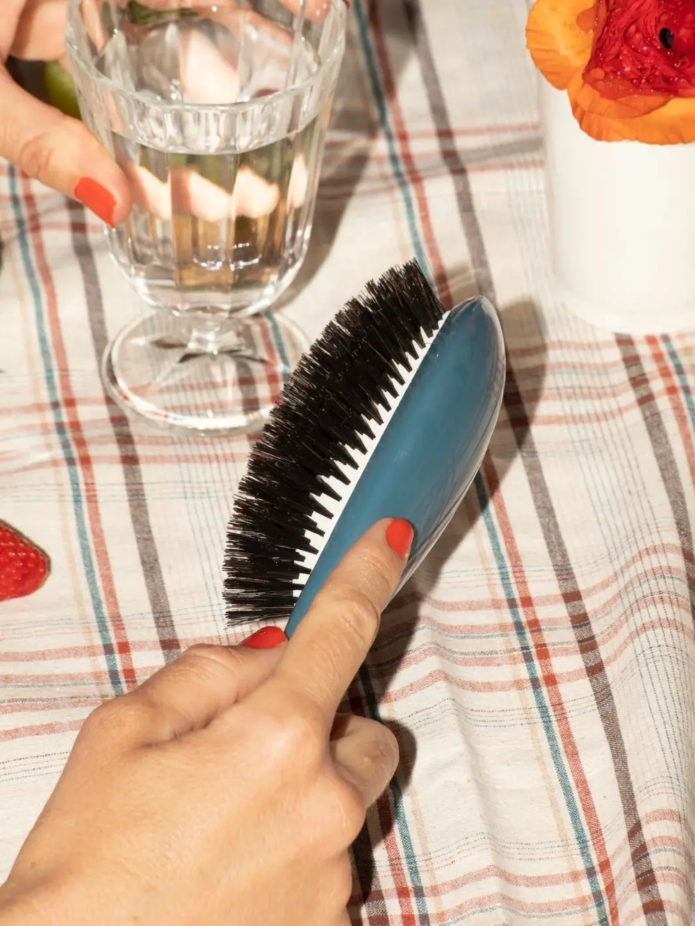 Person holding La Bonne Brosse N.01 The Shine & Care Hairbrush The Universal Brush in Ink Blue held over a patterned tablecloth near a glass of water | Twentyseven Toronto