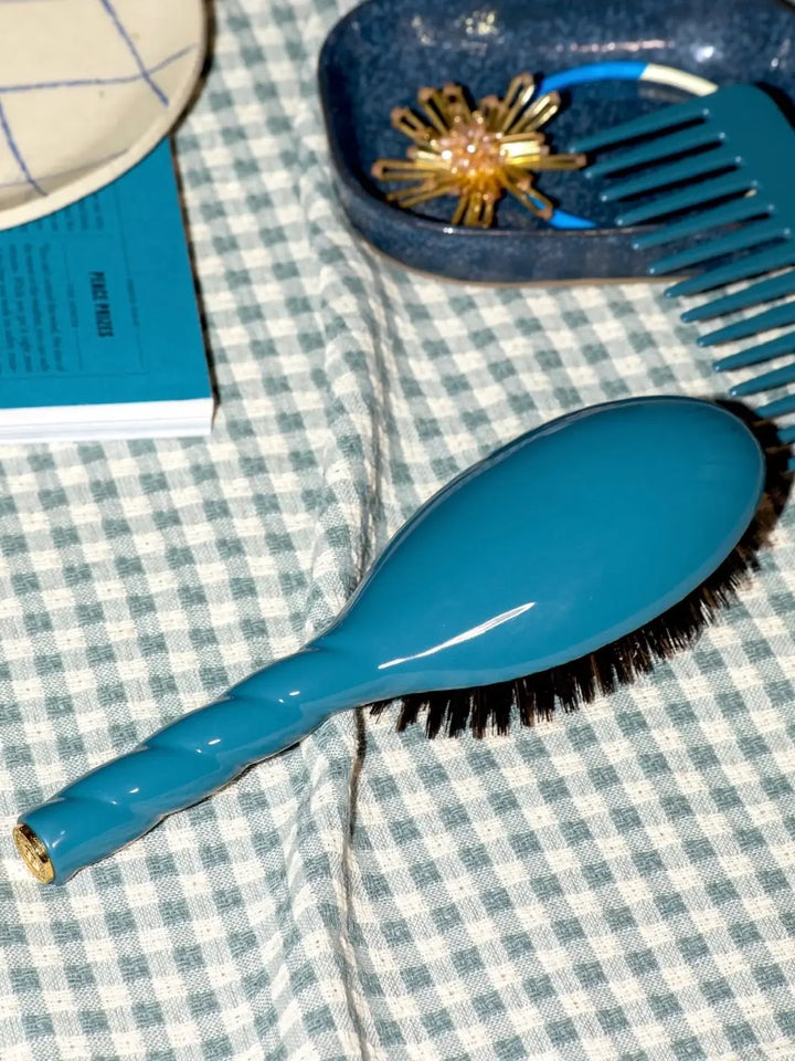 La Bonne Brosse N.01 The Shine & Care Hairbrush The Universal Brush in Ink Blue resting on a checkered surface alongside a blue comb and accessories | Twentyseven Toronto