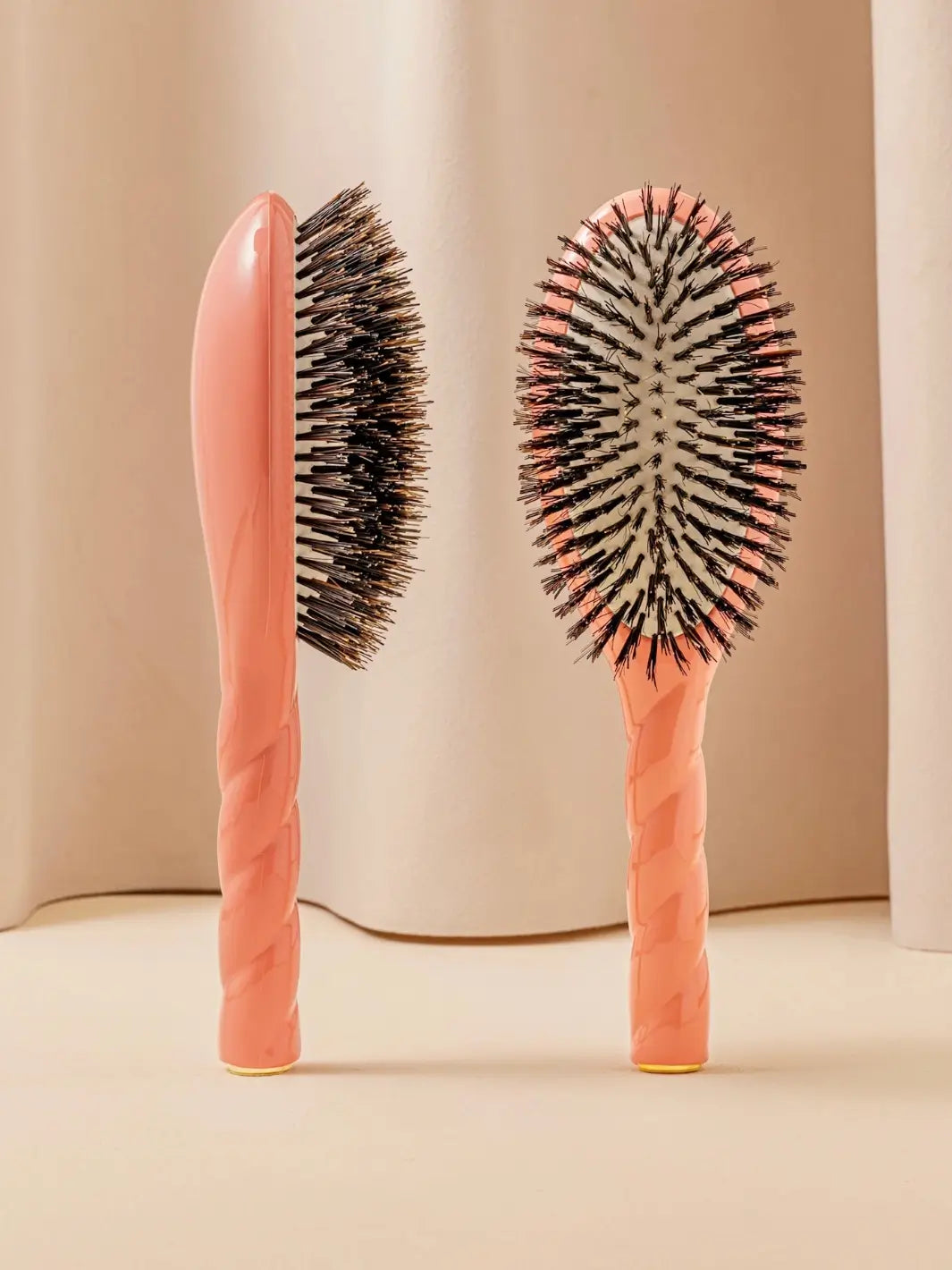 Front and side view of La Bonne Brosse N.01 The Shine & Care Hairbrush The Universal Brush in Orange Coral featuring a twisted ergonomic handle and natural boar bristles | Twentyseven Toronto
