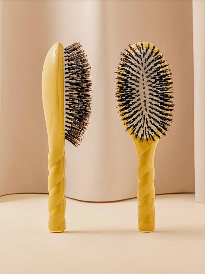 Front and side view of La Bonne Brosse N.01 The Shine & Care Hairbrush The Universal Brush in Saffron Yellow featuring a twisted ergonomic handle and natural boar bristles | Twentyseven Toronto