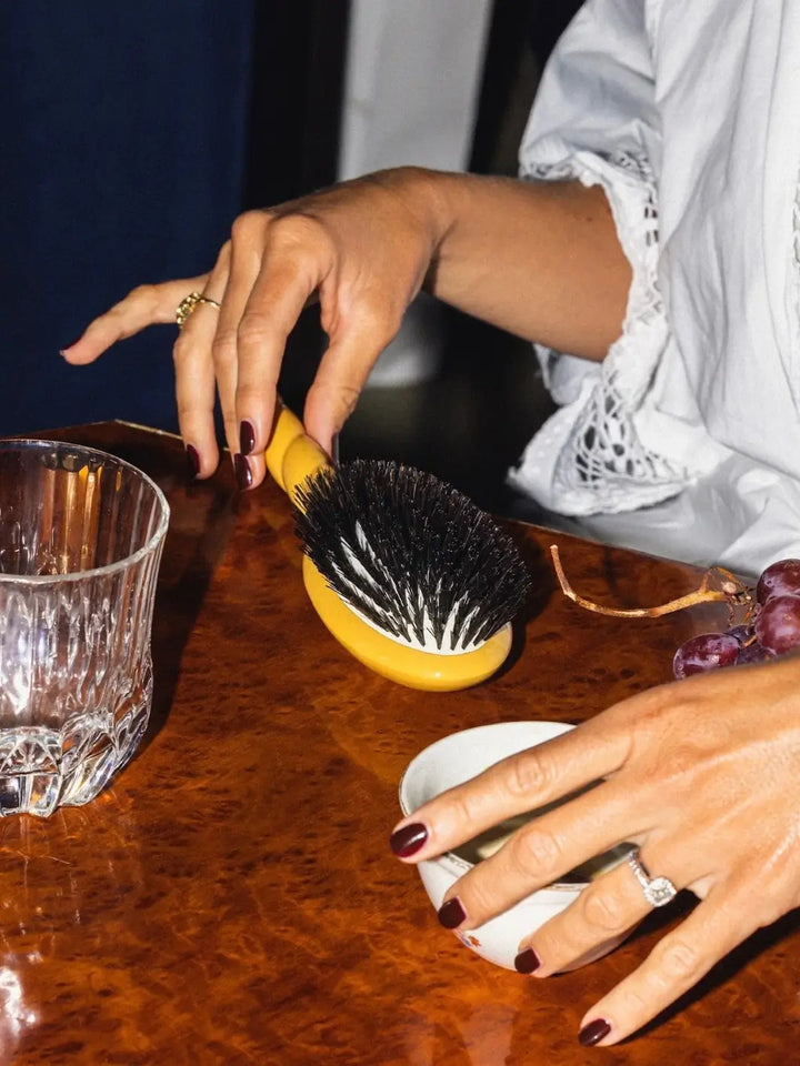 Person holding the La Bonne Brosse N.01 The Shine & Care Hairbrush The Universal Brush in Saffron Yellow resting on a polished wood surface | Twentyseven Toronto