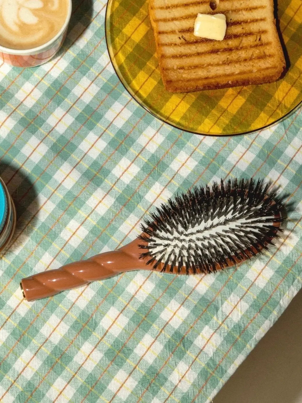 La Bonne Brosse N.01 Large The Shine & Care Hairbrush The Universal Brush in Terracotta is placed on a green and white checkered tablecloth next to a plate of buttered toast and a latte | Twentyseven Toronto