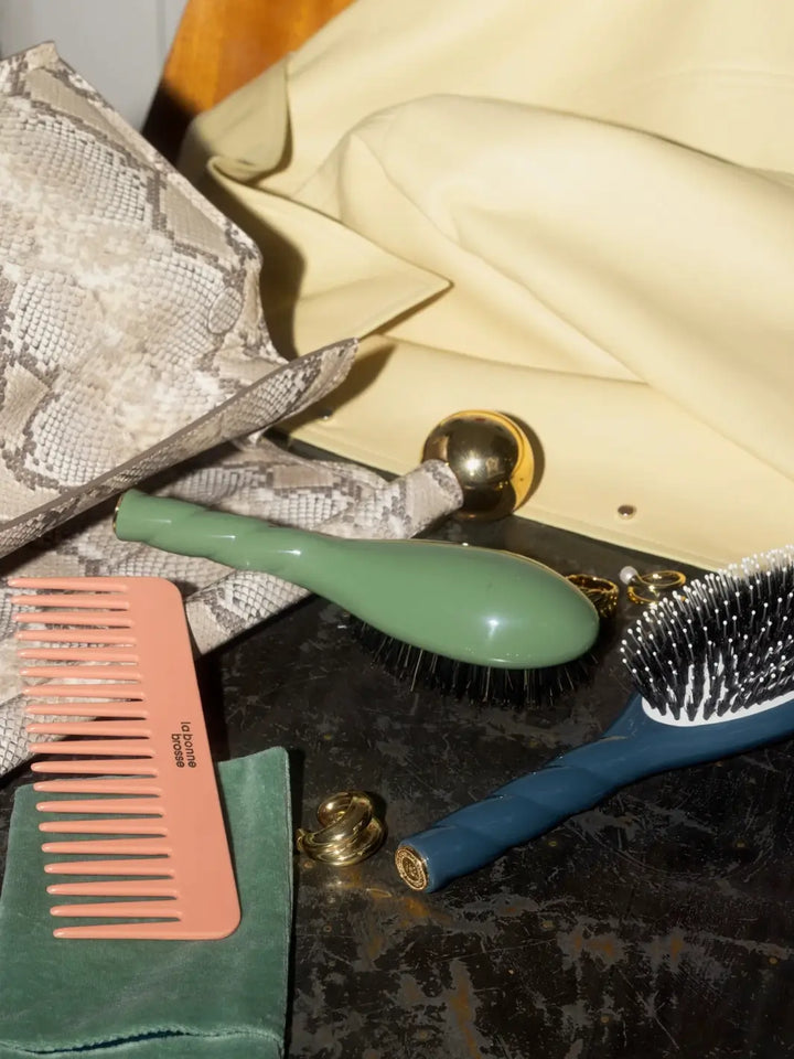 La Bonne Brosse N.01 Small The Shine & Care Hairbrush The Universal Brush in Almond Green is displayed on a dark surface alongside a peach-colored comb, gold jewelry, and a snakeskin-patterned handbag | Twentyseven Toronto