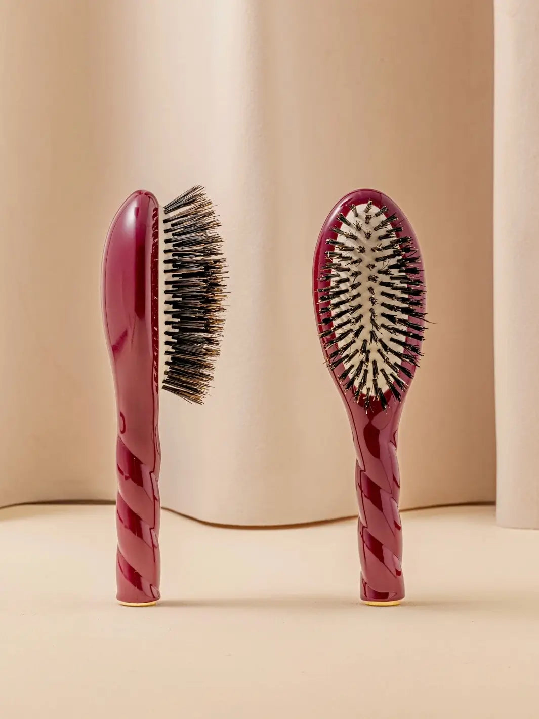 Front and side view of La Bonne Brosse N.01 Small The Shine & Care Hairbrush The Universal Brush in Cherry Red featuring a twisted ergonomic handle and natural boar bristles | Twentyseven Toronto