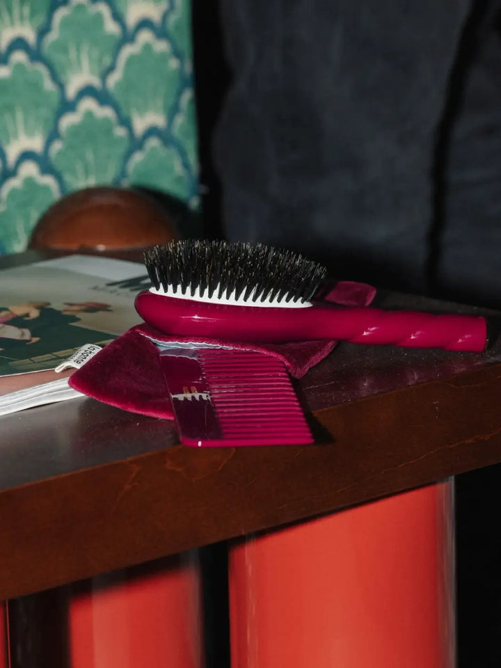 La Bonne Brosse N.01 Small The Shine & Care Hairbrush The Universal Brush in Cherry Red sits on a wooden table alongside a matching comb and a velvet pouch | Twentyseven Toronto
