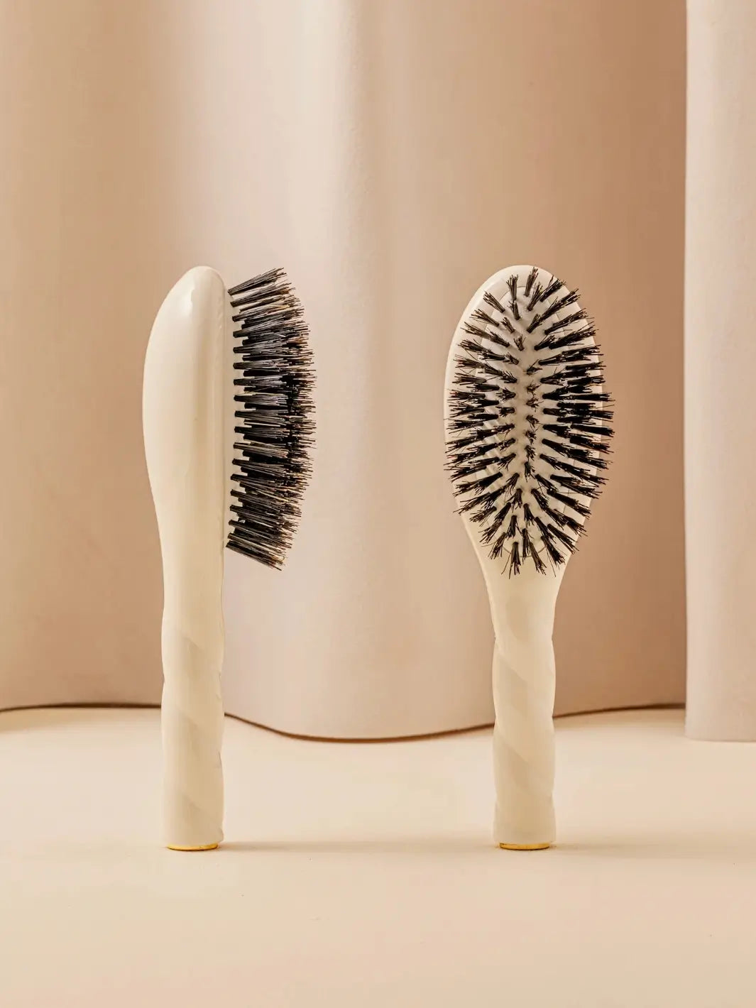 Front and side view of La Bonne Brosse N.01 Small The Shine & Care Hairbrush The Universal Brush in Creamy White featuring a twisted ergonomic handle and natural boar bristles | Twentyseven Toronto