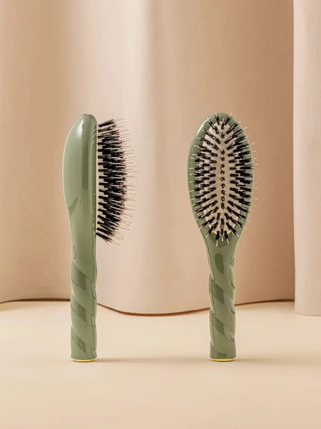 Front and side view of La Bonne Brosse N.02 Small The Essential Detangling & Conditioning Brush in Almond Green featuring a twisted ergonomic handle and natural boar and nylon bristles | Twentyseven Toronto