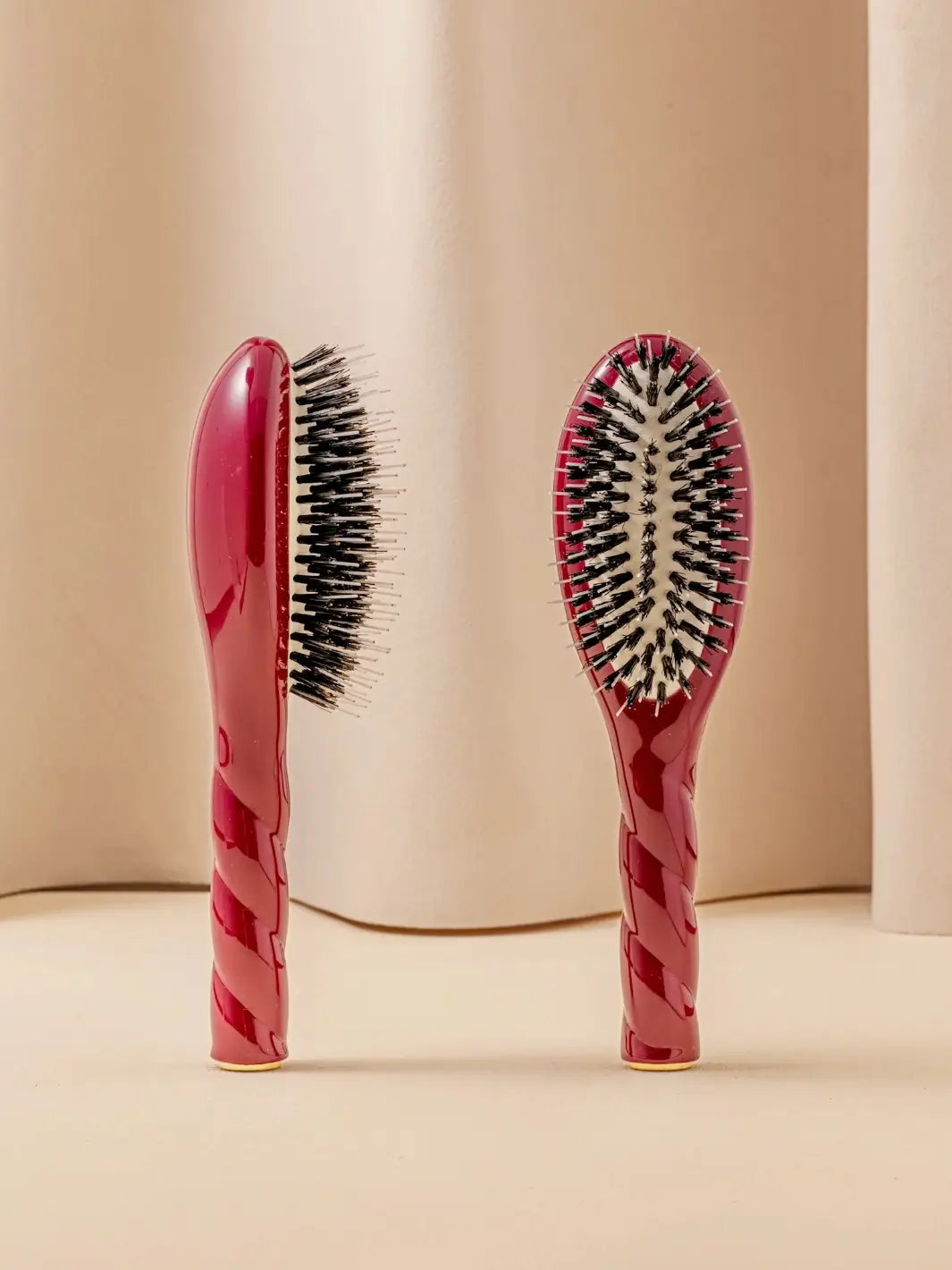 Front and side view of La Bonne Brosse N.02 Small The Essential Detangling & Conditioning Brush in Cherry Red featuring a twisted ergonomic handle and natural boar and nylon bristles | Twentyseven Toronto
