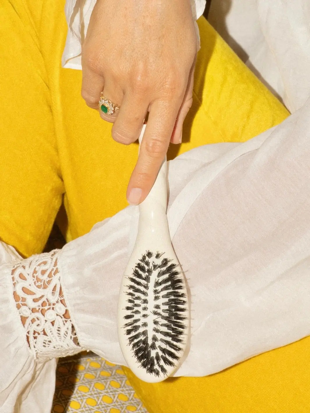 Person wearing a white lace-cuffed blouse and yellow trousers holding the La Bonne Brosse N.02 Small The Essential Detangling & Conditioning Brush in Creamy White | Twentyseven Toronto