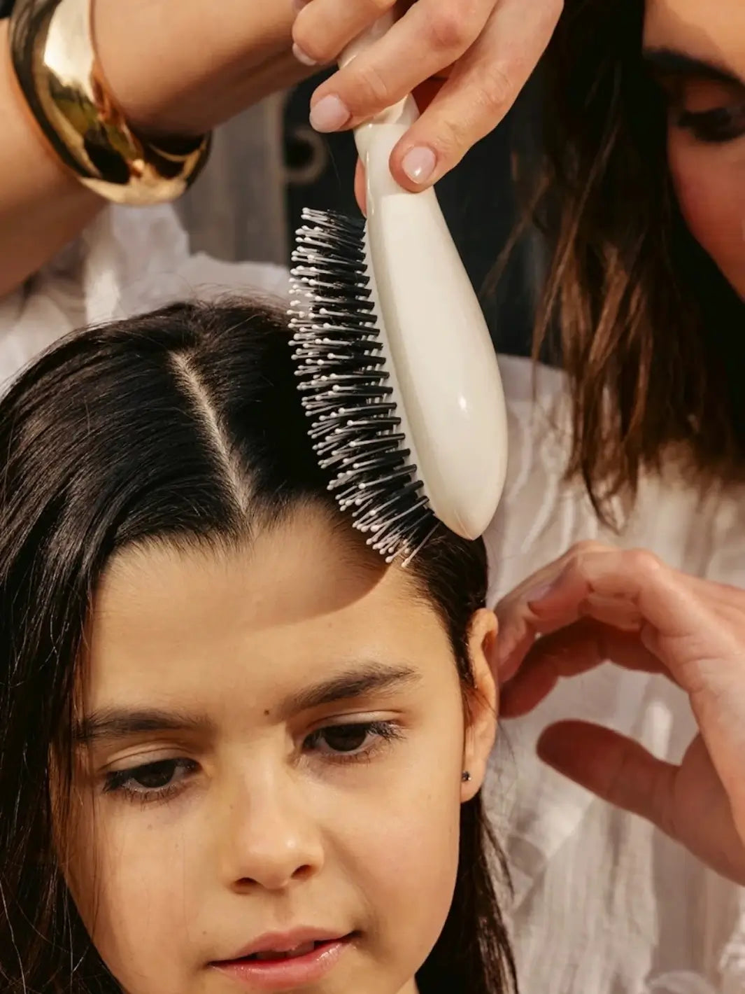 Woman uses the La Bonne Brosse N.03 Large The Essential Softness & Sensitive Scalp Brush in Creamy White to gently style a young girl's dark hair | Twentyseven Toronto