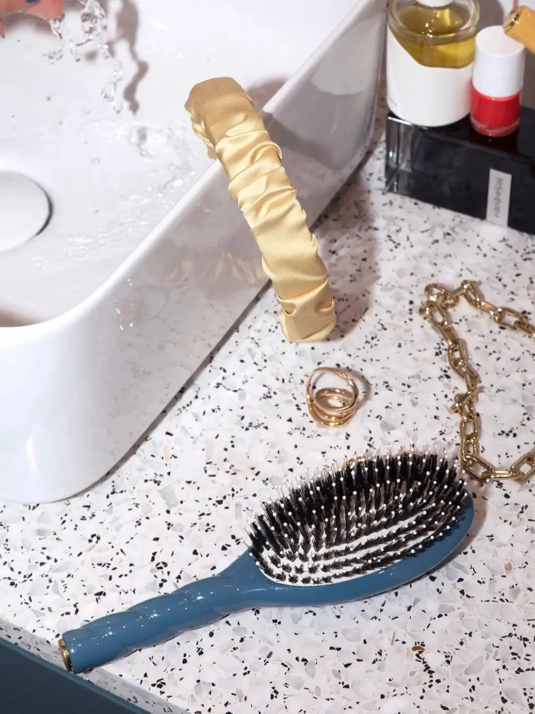 La Bonne Brosse N.03 Large The Essential Softness & Sensitive Scalp Brush in Ink Blue laying on a speckled countertop next to a white sink, gold jewelry, and a yellow silk headband | Twentyseven Toronto