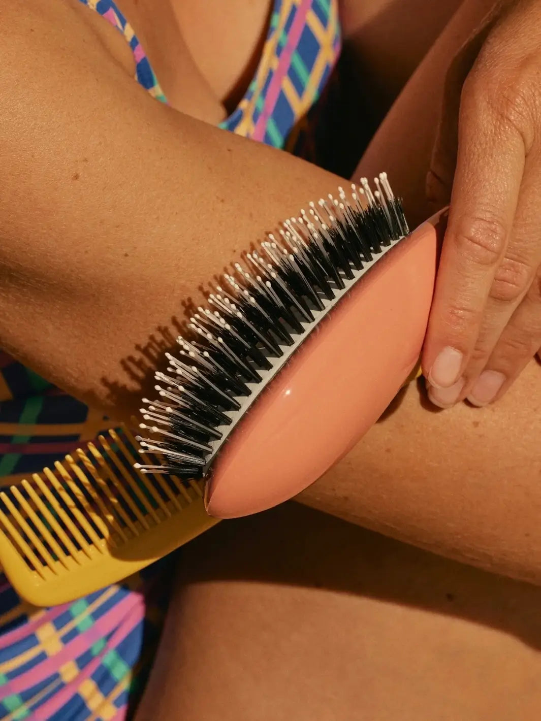 Hand holding the La Bonne Brosse N.03 Large The Essential Softness & Sensitive Scalp Brush in Orange Coral next to a yellow comb | Twentyseven Toronto
