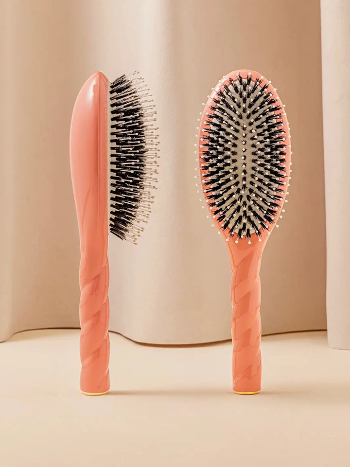 Front and side view of La Bonne Brosse N.03 Large The Essential Softness & Sensitive Scalp Brush in Orange Coral featuring a twisted ergonomic handle and natural boar bristles | Twentyseven Toronto