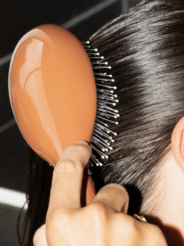Person using the La Bonne Brosse N.03 Large The Essential Softness & Sensitive Scalp Brush in Terracotta to smooth through sleek, dark hair | Twentyseven Toronto