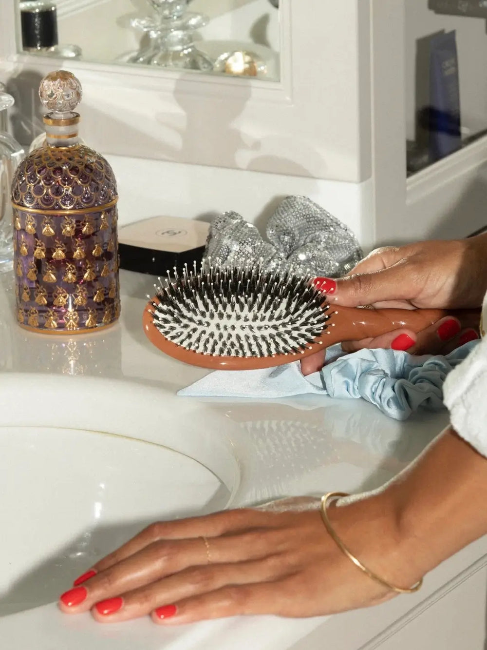 Hand with red nails holding the La Bonne Brosse N.03 Large The Essential Softness & Sensitive Scalp Brush in Terracotta over a white bathroom vanity | Twentyseven Toronto