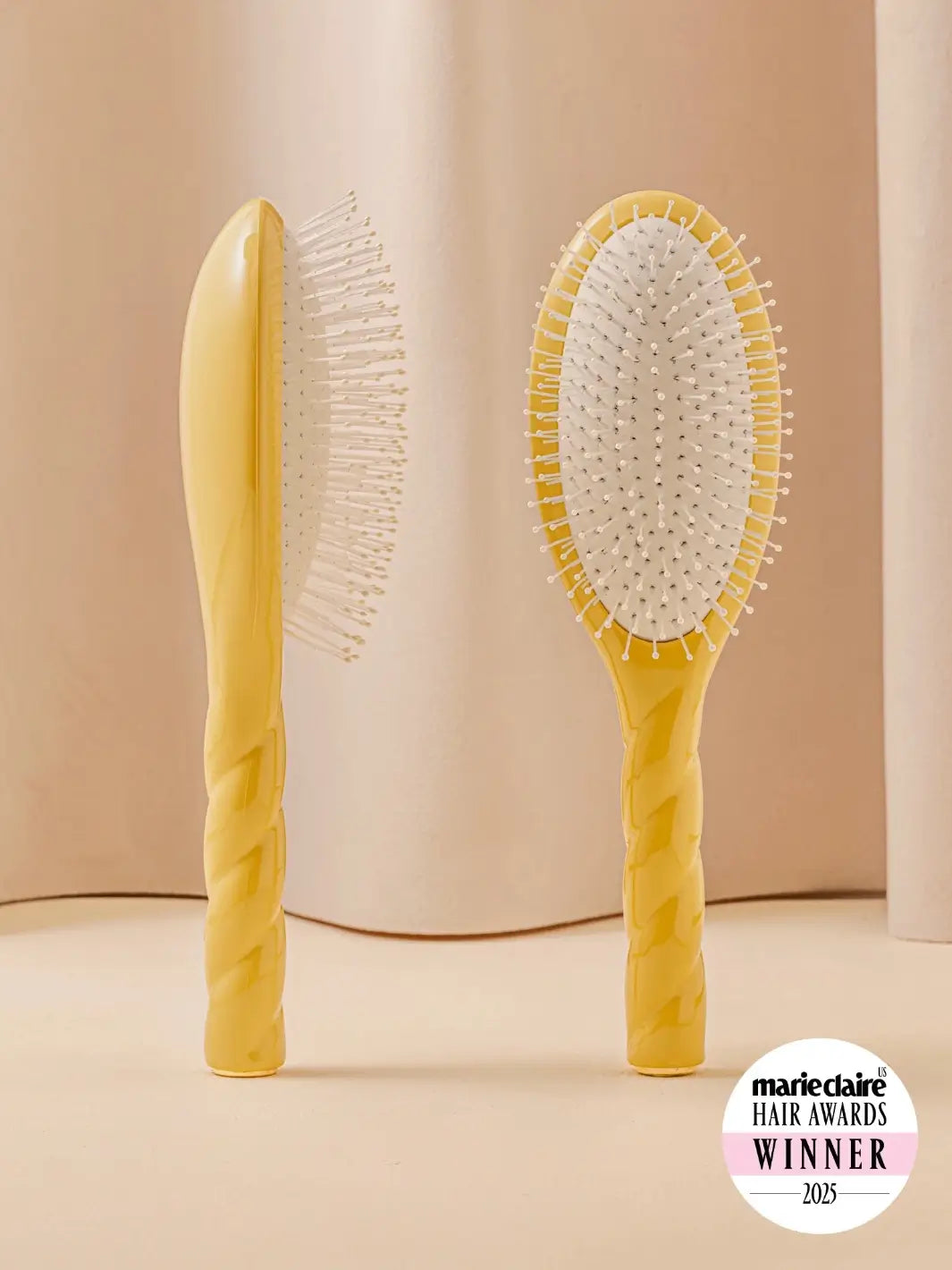 Front and side view of La Bonne Brosse N.04 Large The Detangling & Massaging Miracle Brush in Saffron Yellow featuring a twisted ergonomic handle and nylon bristles | Twentyseven Toronto