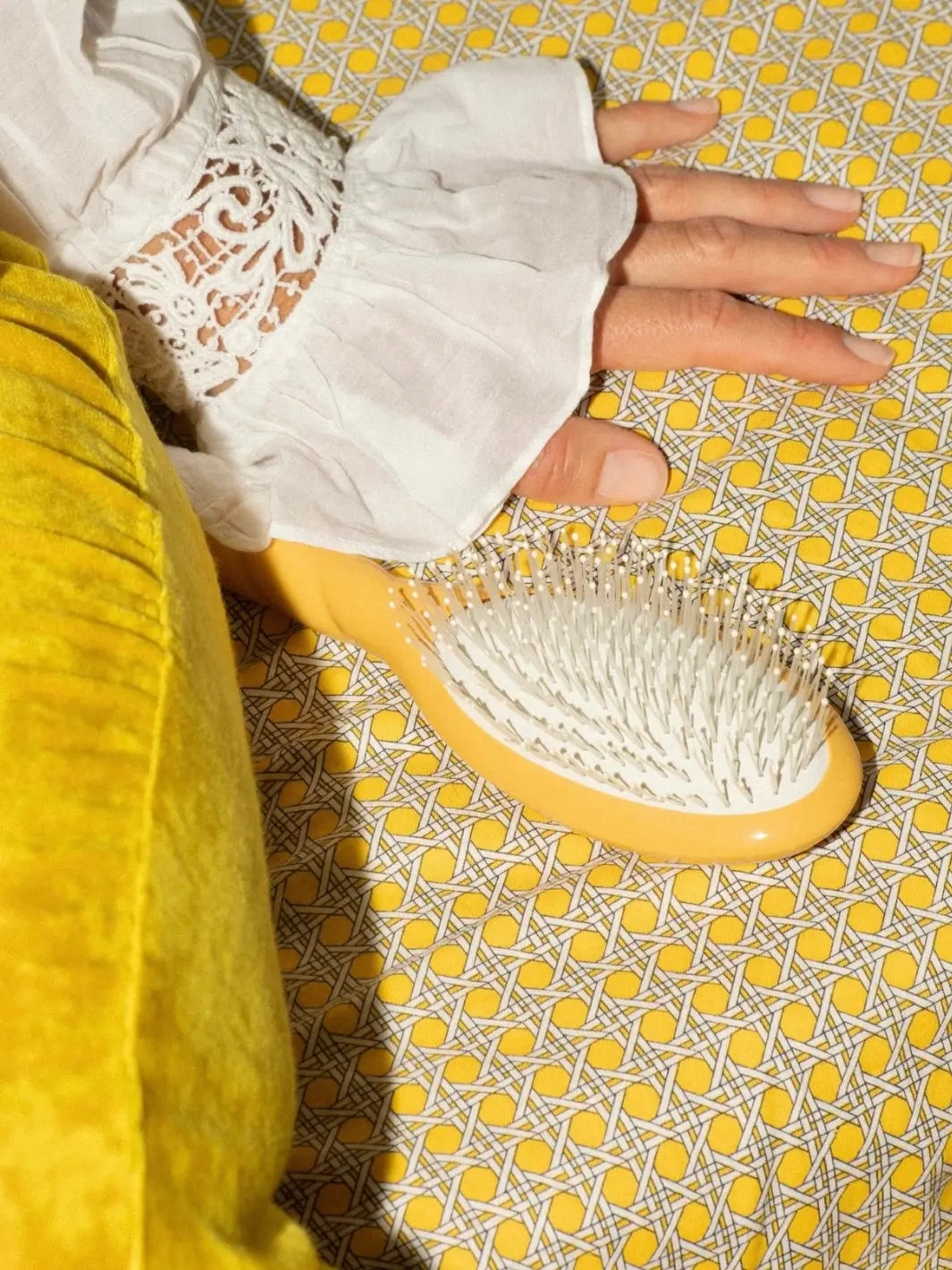 La Bonne Brosse N.04 Large The Detangling & Massaging Miracle Brush in Saffron Yellow on a yellow patterned surface next to a hand in a white lace sleeve | Twentyseven Toronto