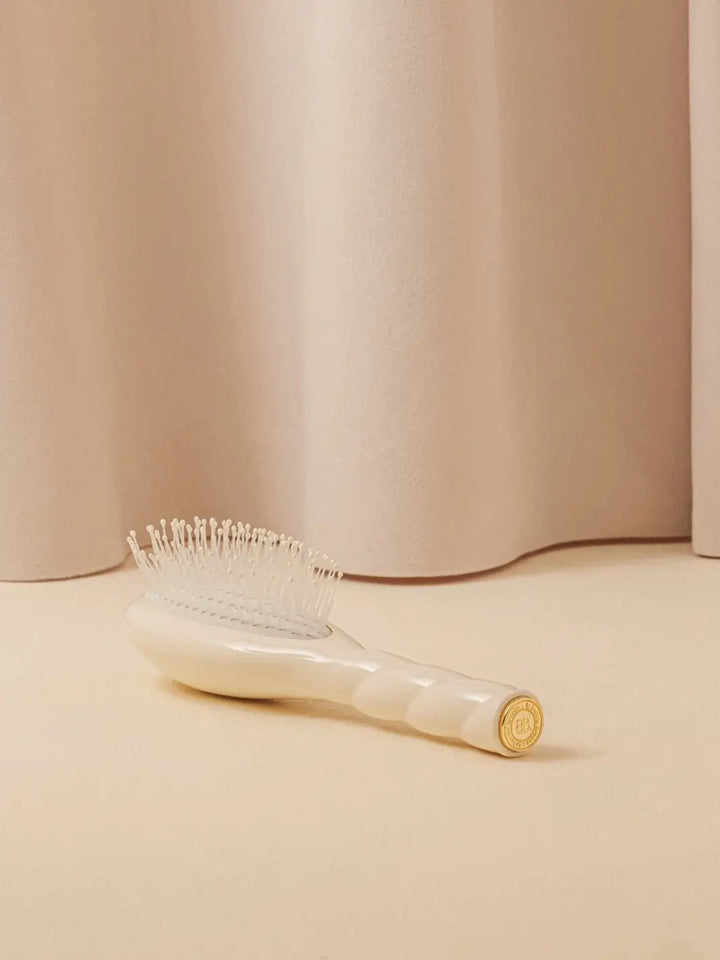 La Bonne Brosse N.04 Small The Detangling & Massaging Miracle Brush in Creamy White resting on a neutral surface against a soft draped curtain background | Twentyseven Toronto