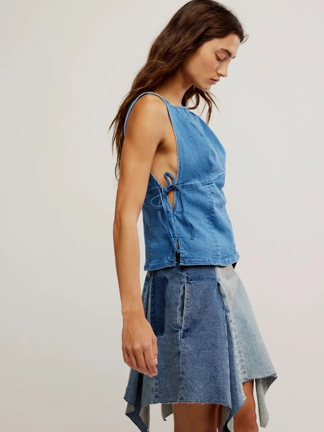 A side profile view highlights the structured sleeveless design and curved hemline of the Free People Not My Fault Corset - Denim Baby Blue styled with a patchwork denim skirt | Twentyseven Toronto