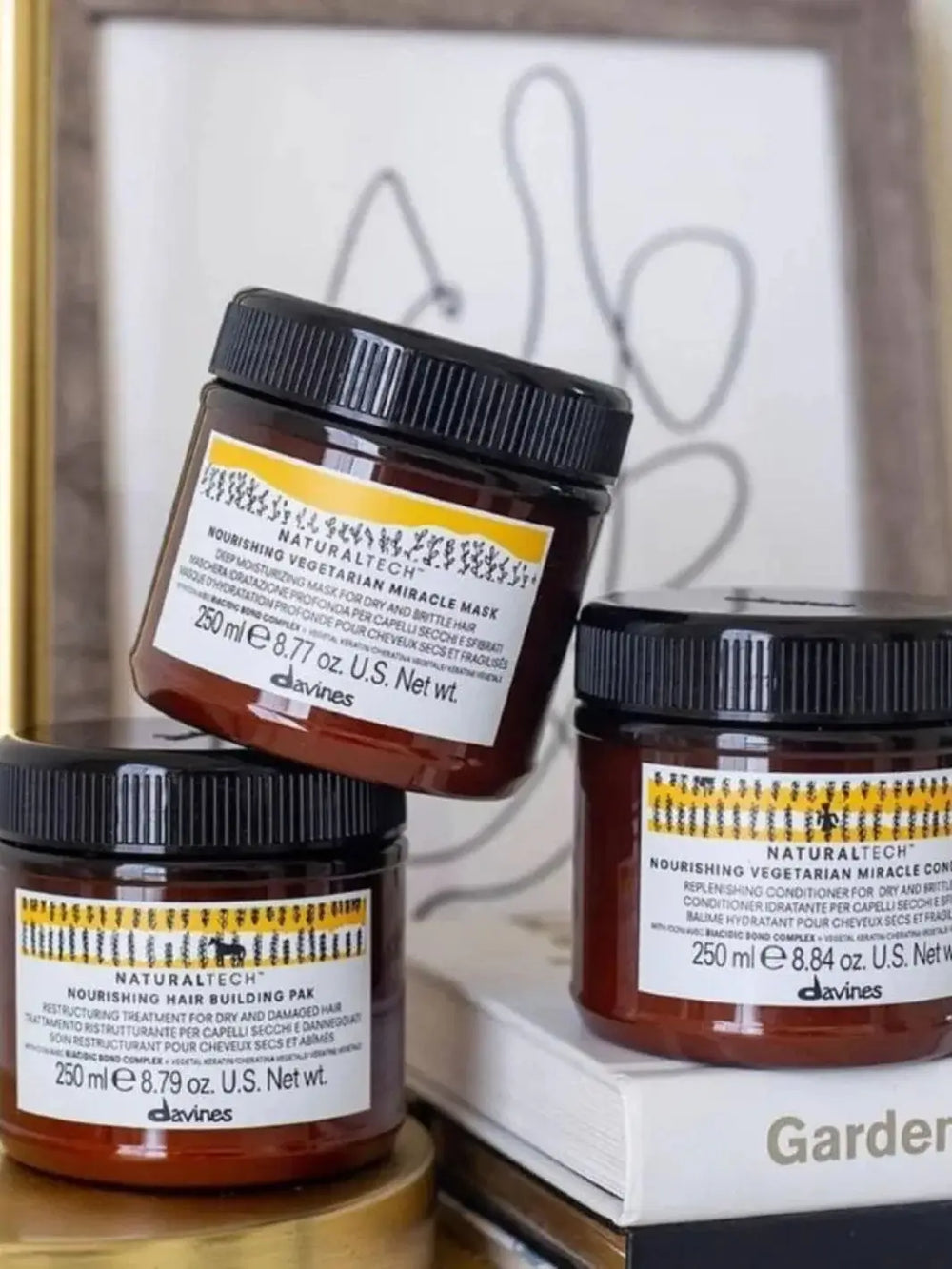  A stack of three amber jars features the Davines NOURISHING Vegetarian Miracle Mask arranged alongside other Naturaltech hair products against a blurred background | Twentyseven Toronto
