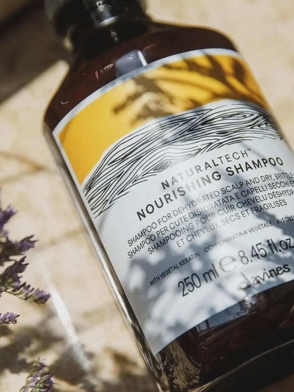 An angled, close-up shot shows a bottle of Davines NOURISHING Shampoo outdoors with shadows across its yellow and white label | Twentyseven Toronto