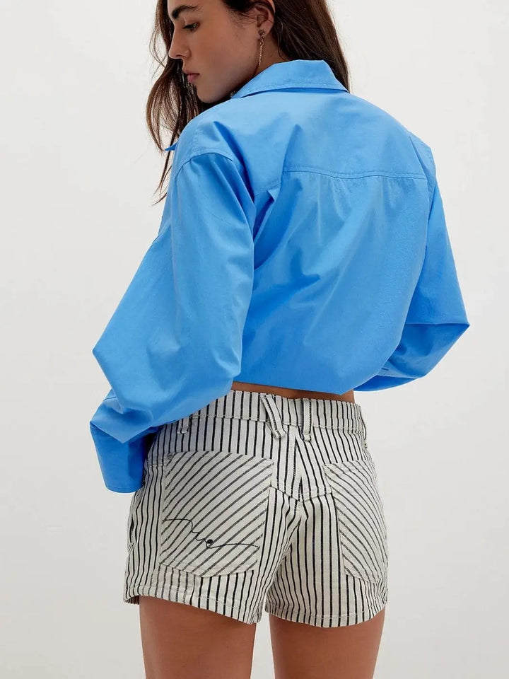 A back view details the fit, belt loops, and distinct back pocket design of the Free People Now Or Never Railroad Denim Shorts - Washed Railroad paired with a tucked-in blue shirt | Twentyseven Toronto