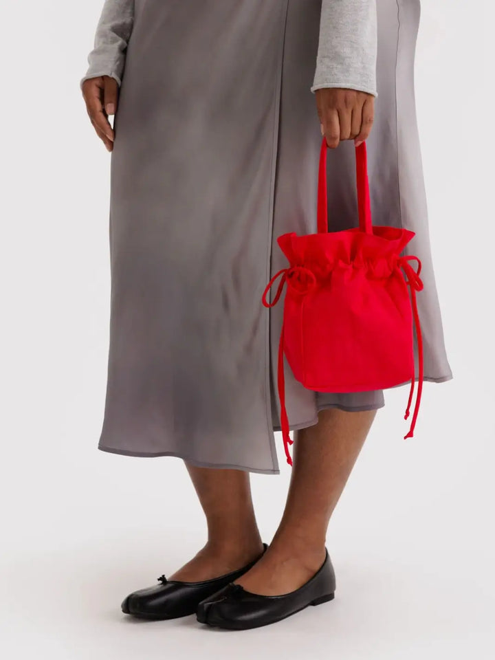 Person holds the BAGGU Nylon Drawstring Bag in Candy Apple by its top handles | Twentyseven Toronto