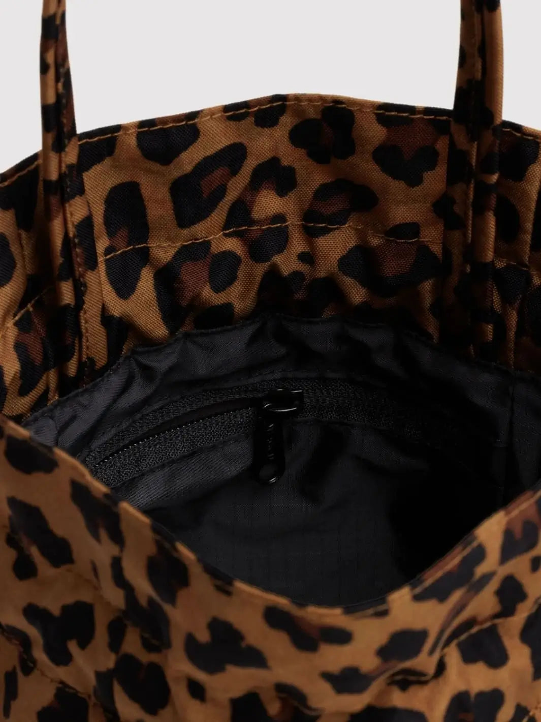 A close-up view looking into the interior of a Baggu Nylon Drawstring Bag in Leopard, revealing a black lining and an inner zippered pocket | Twentyseven Toronto