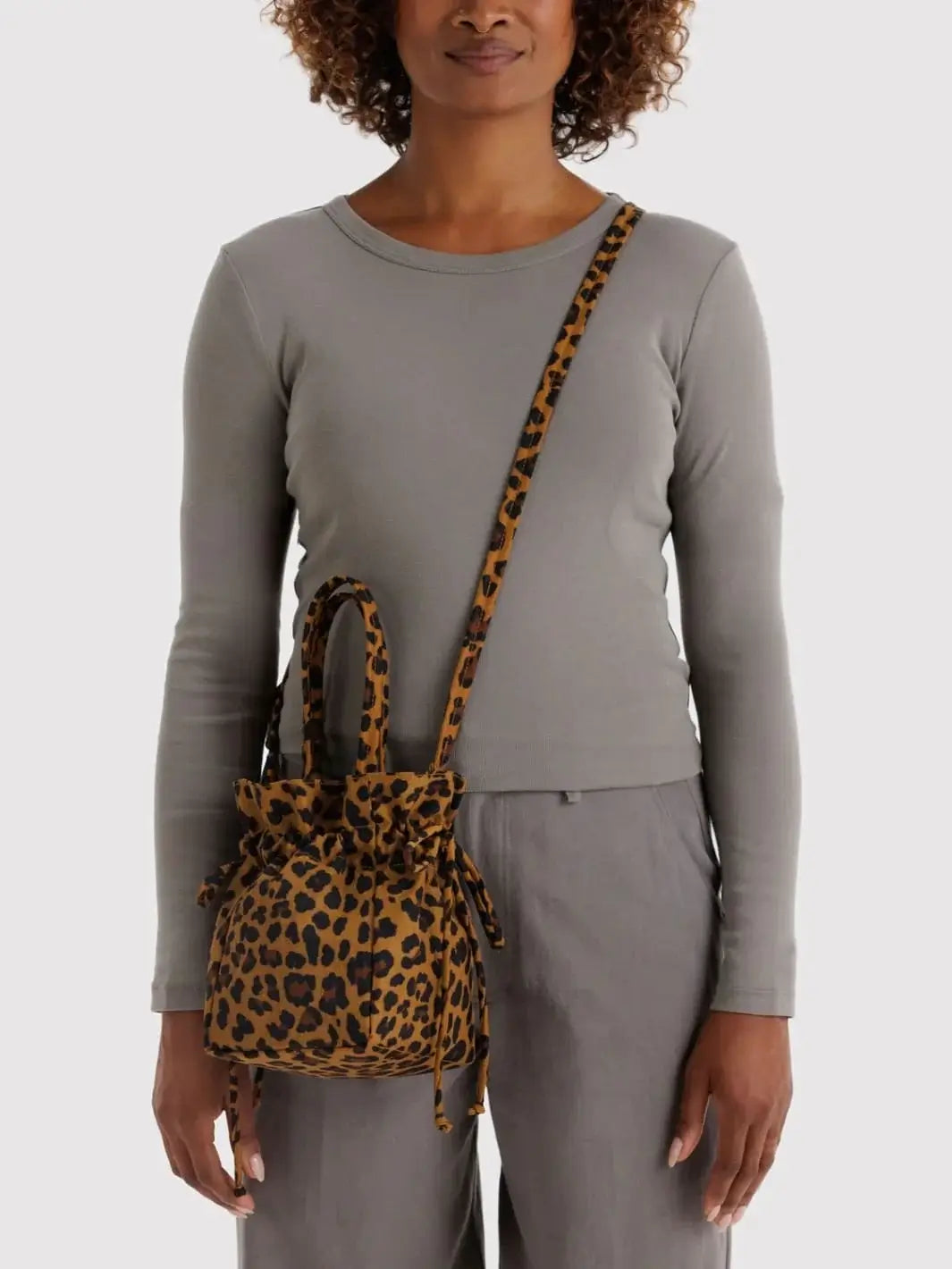 A front-facing view of a person wearing a grey long-sleeve shirt and matching trousers, sporting a Baggu Nylon Drawstring Bag in Leopard across the body with its long shoulder strap | Twentyseven Toronto