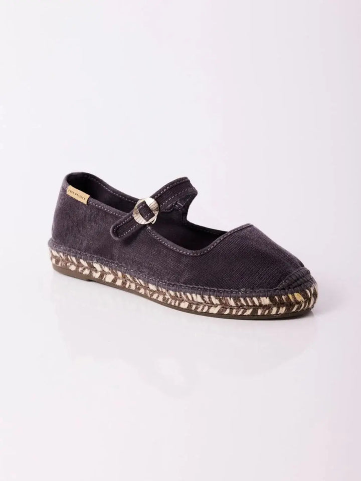 A three-quarter studio view showcases a single Free People Oasis Mary Jane Espadrilles - Washed Black resting on a reflective white surface | Twentyseven Toronto