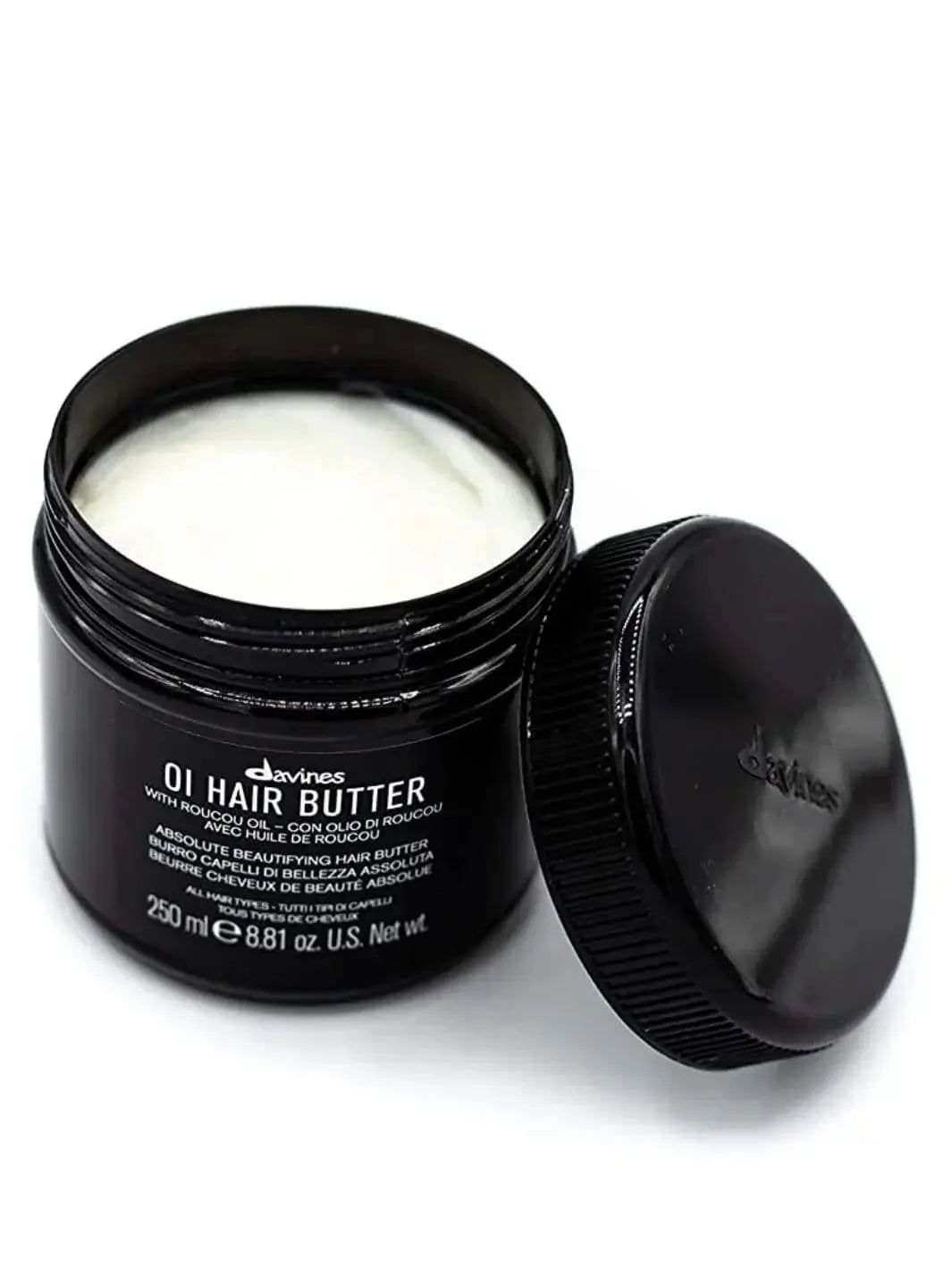 An open black jar displays the thick white cream of the Davines OI Hair Butter Mask with its lid leaning against the side | Twentyseven Toronto