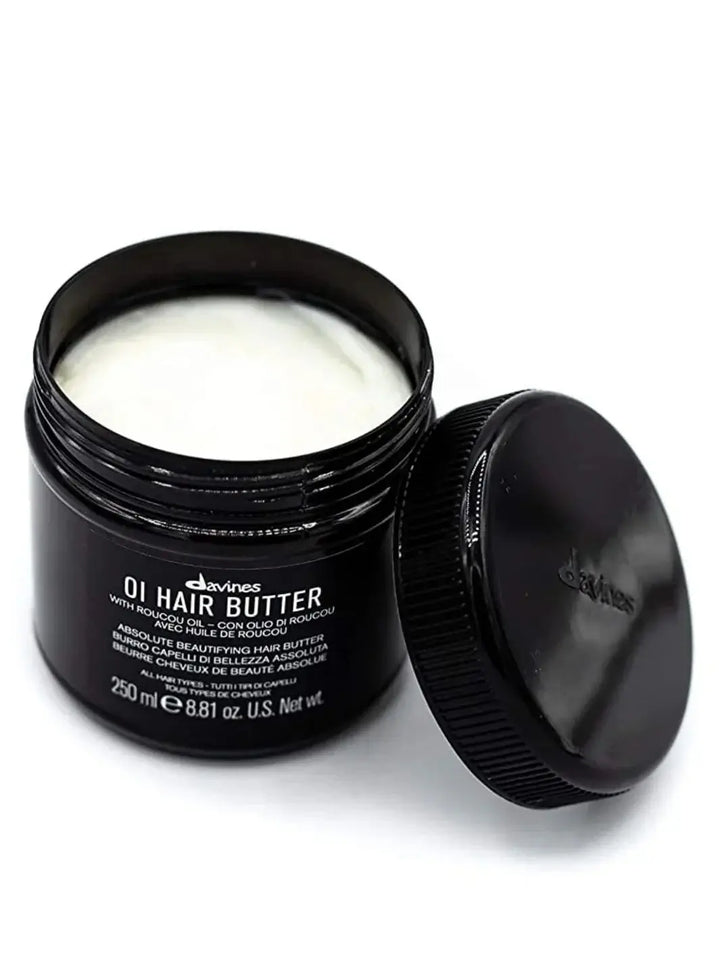 An open black jar displays the thick white cream of the Davines OI Hair Butter Mask with its lid leaning against the side | Twentyseven Toronto