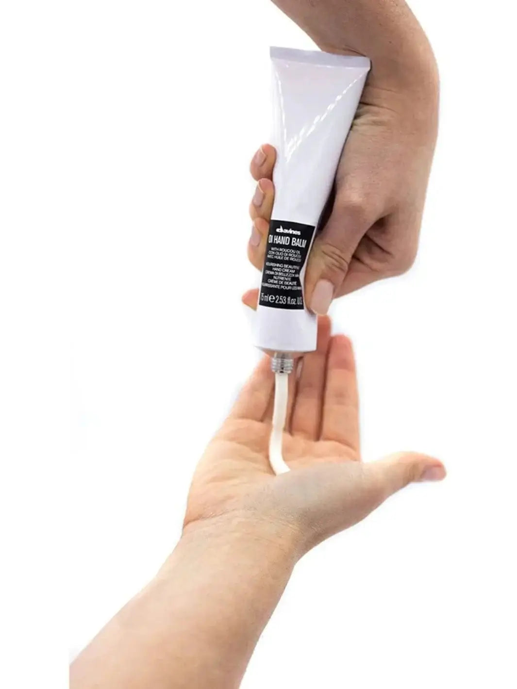 A hand squeezes white cream from a tube of OI Hand Balm directly into another open palm against a white background | Twentyseven Toronto