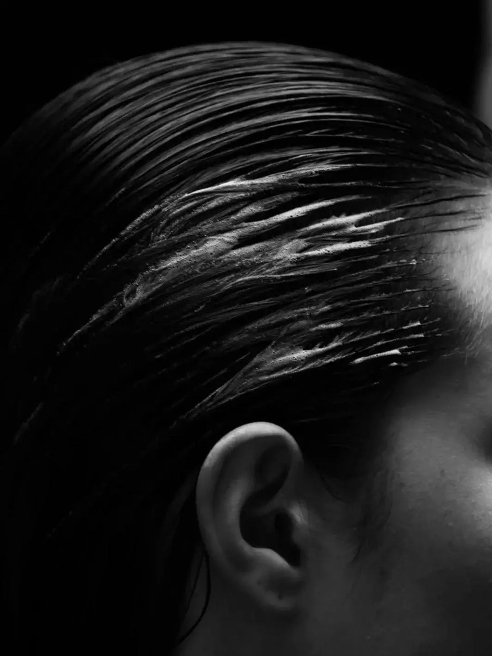 A black and white close-up shows wet hair slicked back away from a person's ear after applying Davines OI Soufflé | Twentyseven Toronto