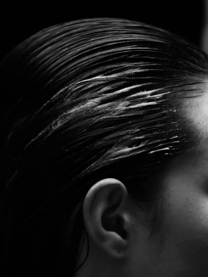 A black and white close-up shows wet hair slicked back away from a person's ear after applying Davines OI Soufflé | Twentyseven Toronto