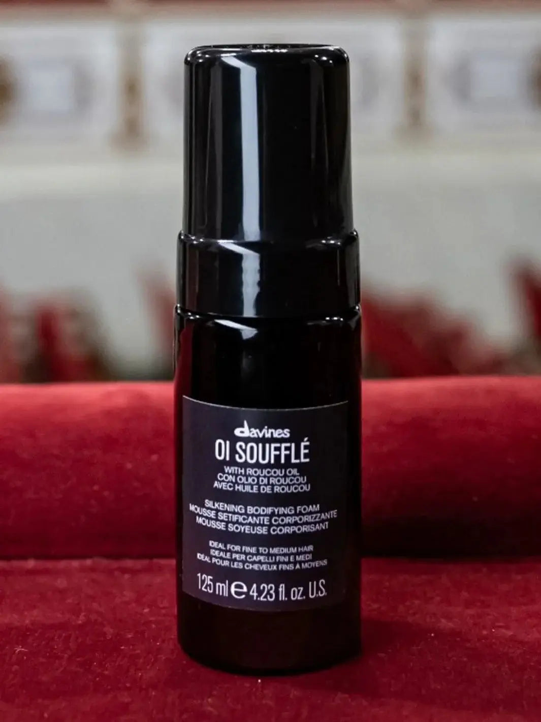 A black bottle of Davines OI Soufflé on a textured red fabric surface with a blurred background | Twentyseven Toronto