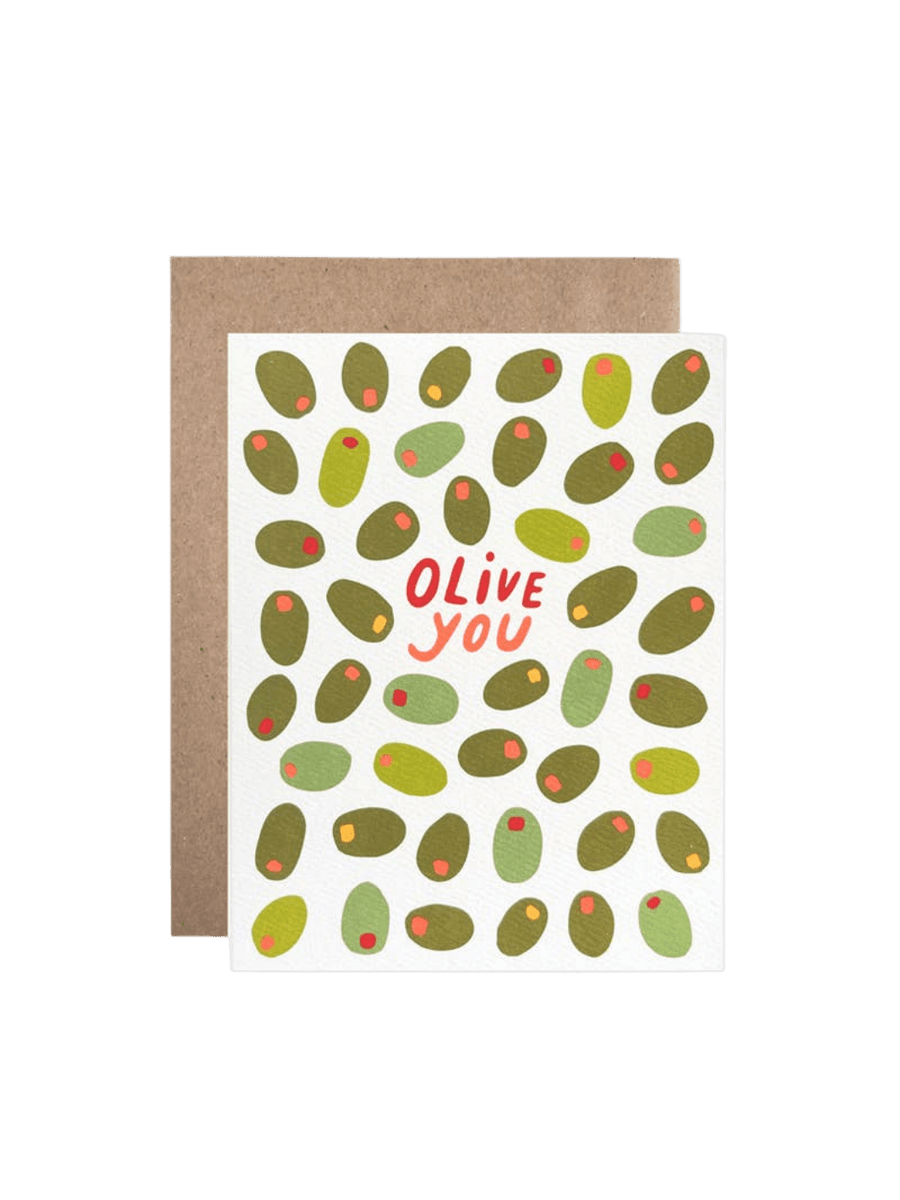 The Hartland Cards Olive You Card features a white background covered in a pattern of various green olives with red pimento centers, with the words "Olive you" written in red playful font in the middle, resting in front of a brown kraft envelope | Twentyseven Toronto