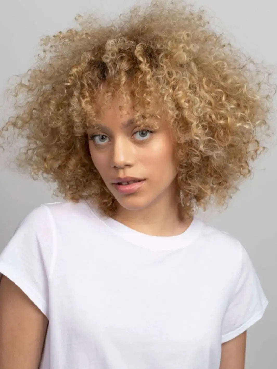 A portrait of a model showcasing soft, voluminous blonde curls that have been hydrated and styled with R+Co ON A CLOUD Repair Mask | Twentyseven Toronto