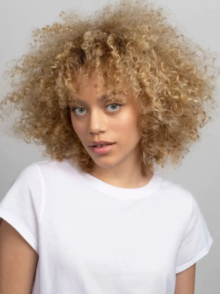 A portrait of a model showcasing soft, voluminous blonde curls that have been hydrated and styled with R+Co ON A CLOUD Repair Mask | Twentyseven Toronto