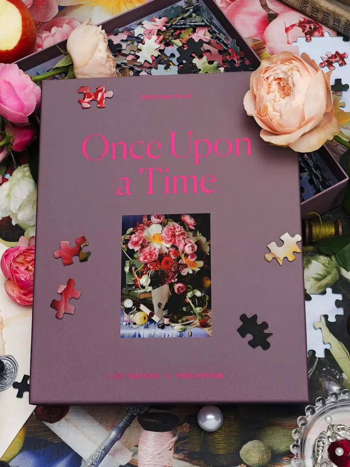 Puzzle box from Piecework Puzzles titled 'Once Upon a Time' 1000 piece puzzle surrounded by roses and puzzle pieces on a table | Twentyseven Toronto