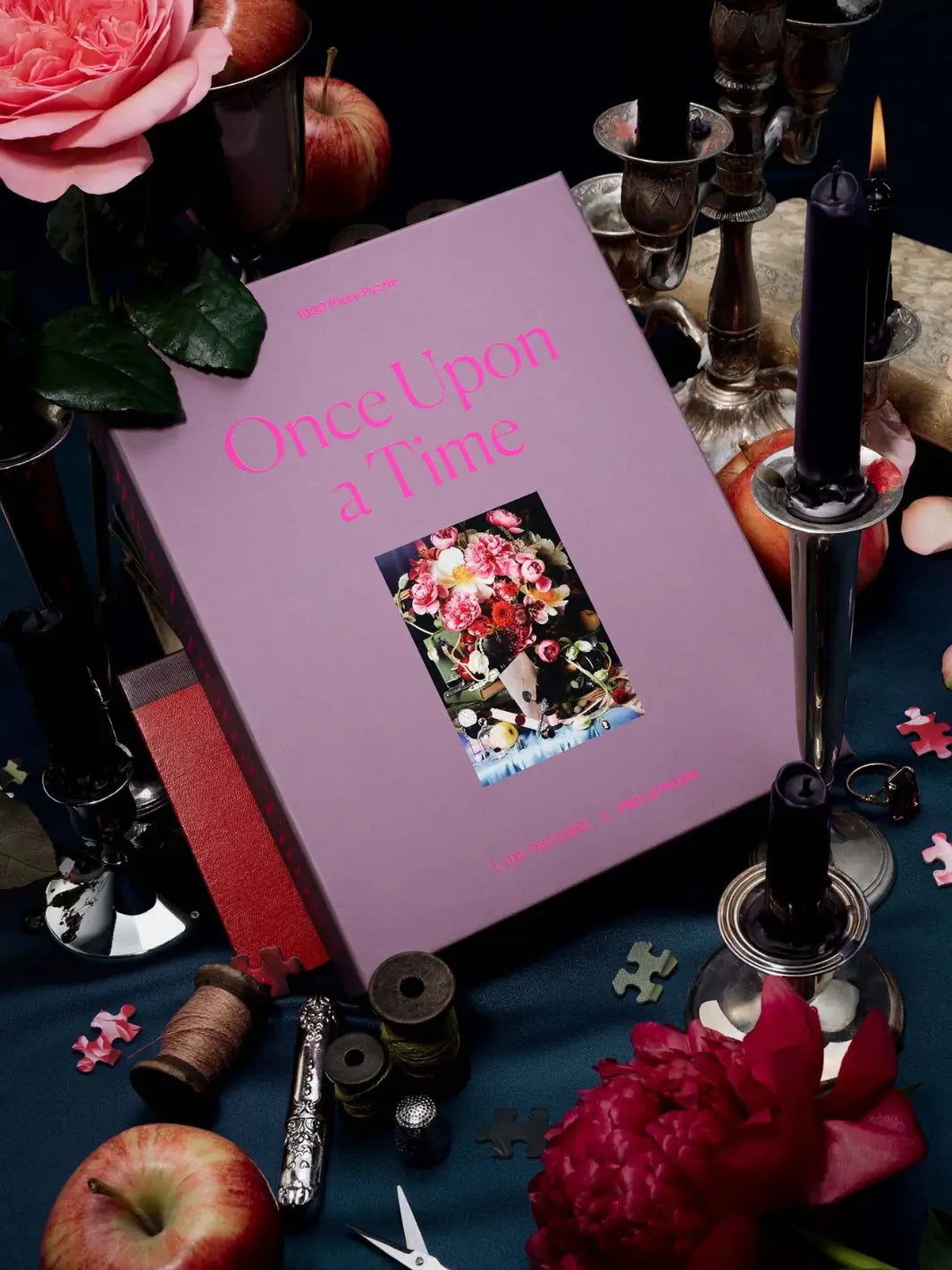 Purple jigsaw puzzle packaging titled 'Once Upon a Time' 1000 piece puzzle from Piecework Puzzles surrounded by candles and flowers on a dark surface | Twentyseven Toronto