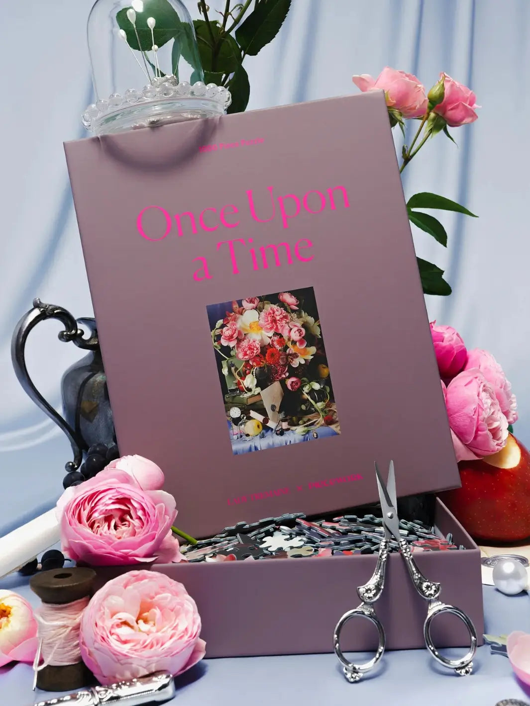 Purple jigsaw puzzle packaging labeled 'Once Upon a Time' 1000 piece puzzle by Piecework Puzzles with floral decorations and vintage scissors on a light blue background | Twentyseven Toronto