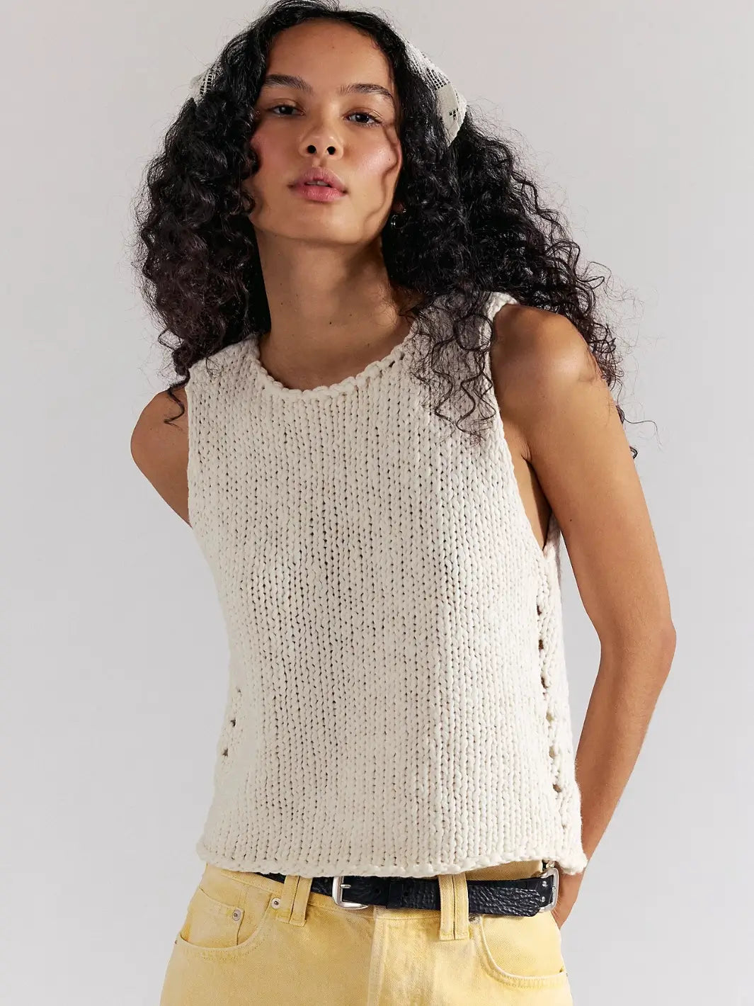 A woman with long, curly dark hair poses from the front wearing yellow denim shorts and the textured, sleeveless Free People Opal Knit Tank in Whisper White | Twentyseven Toronto