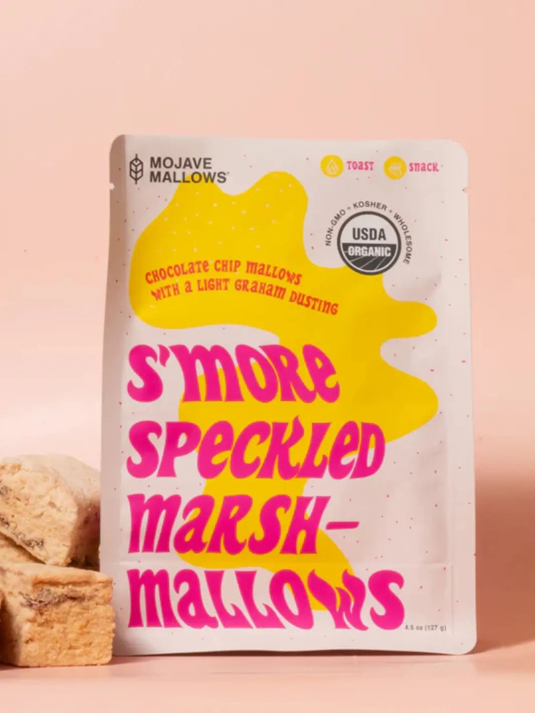 A package of Mojave Mallows Organic S'more Speckled Marshmallows featuring bold pink text on a bright yellow splat background, with square marshmallows stacked next to it | Twentyseven Toronto
