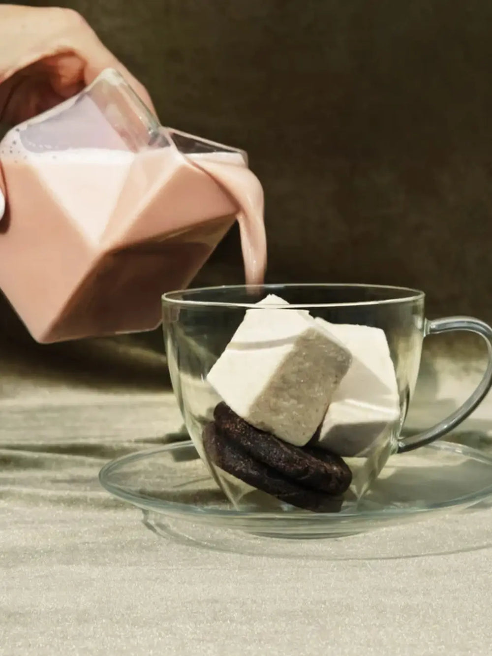 A hand pours chocolate milk from a geometric glass carton into a clear mug filled with cookies and Mojave Mallows Organic Vanilla Bean Marshmallows | Twentyseven Toronto